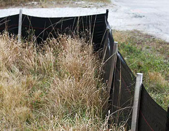 Silt fence installation in a grassy area to control sediment and prevent erosion, supported by wooden stakes.